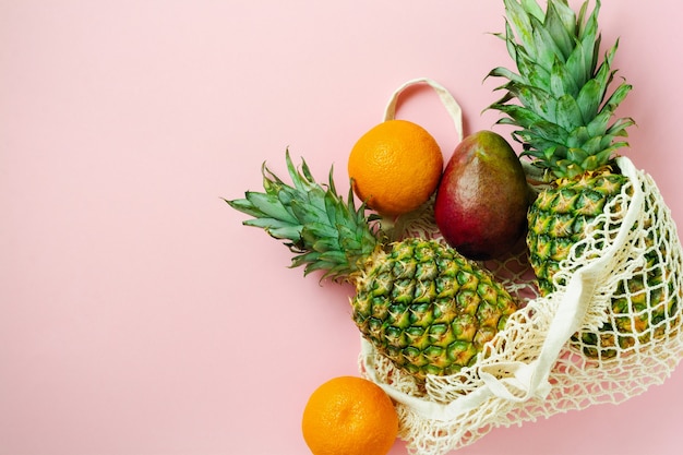 Frutas frescas abacaxi, laranja e manga em uma sacola de compras de malha na cor rosa