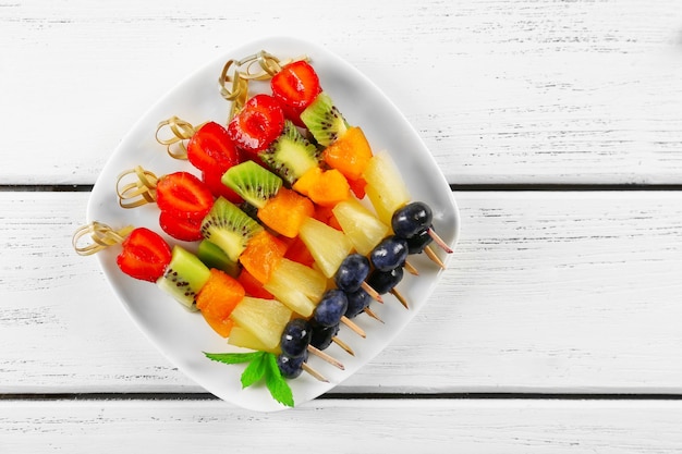 Foto frutas frescas en brochetas en plato en la vista superior de la mesa de madera