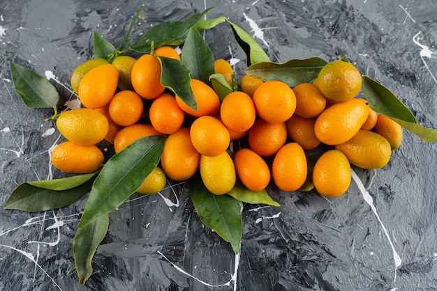 Frutas frescas de cumquat con hojas colocadas sobre una mesa de mármol.