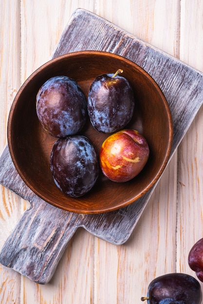 Frutas frescas de ameixa doce em uma tigela de madeira marrom na velha tábua de corte, mesa de madeira, vista superior