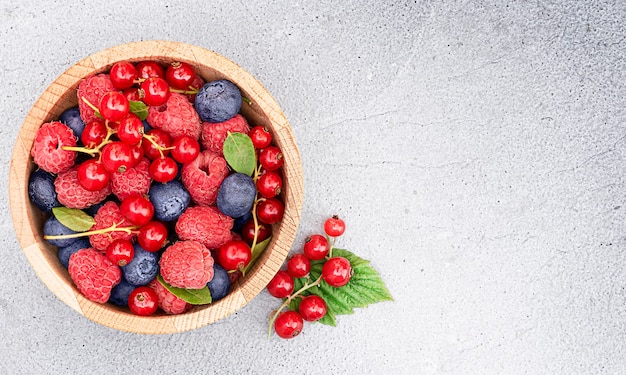Frutas frescas de framboesa, groselha e mirtilo em um prato sobre um fundo claro de concreto