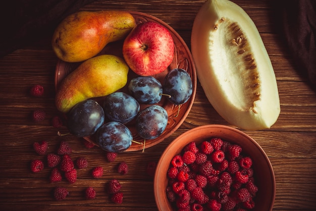 Frutas frescas de outono mentem sobre uma mesa de madeira. Colheita de frutas frescas na mesa. Maçãs frescas, peras, ameixas, framboesas, melão em cima da mesa.