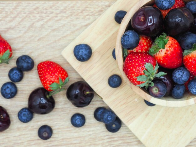 Frutas frescas do verão, cereja, morango e mirtilo na bacia de madeira isolada no fundo de madeira.