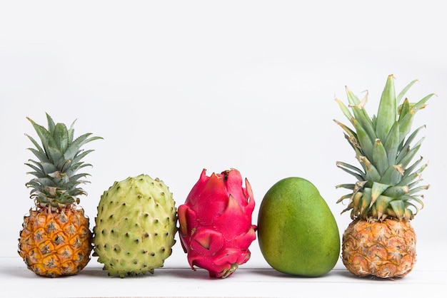 Frutas frescas exóticas del verano en blanco. La fruta del dragón, la piña, el caqui, el mango, la annona cherimola yacían planas con espacio de copia libre.