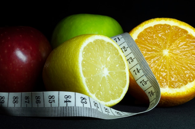 Frutas frescas: maçãs, laranja fatiada e limão com fita métrica