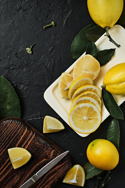 Frutas frescas maduras de limão amarelo e metades de limão com folhas. Vista superior das frutas em um fundo escuro de pedra. Corte a tábua com uma faca, cortando os cítricos em fatias.