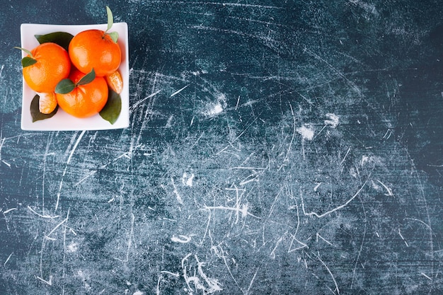 Frutas frescas de mandarina enteras con hojas colocadas en un plato blanco.