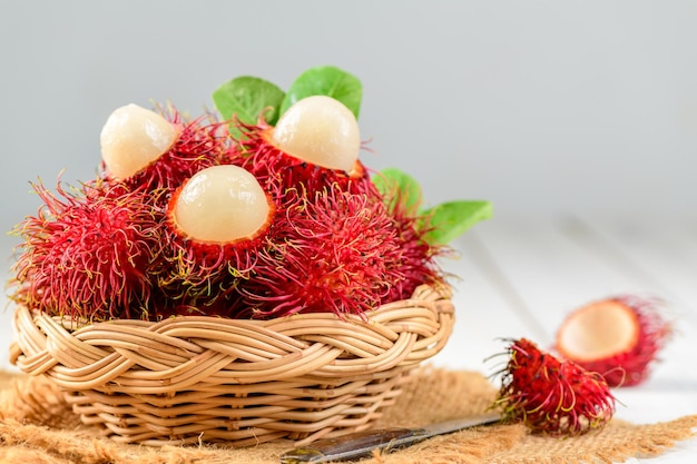 Frutas frescas de rambután con hojas en cesta de bambú sobre fondo de madera