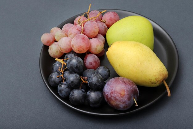 Frutas frescas uva ciruela manzana pera en el plato