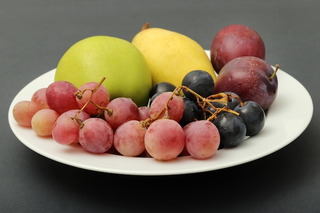 Frutas frescas uva ciruela manzana pera en el plato