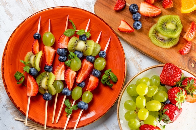 Frutas frescas de verano en palos. Fresas, uvas, arándanos y kiwi en una presentación original. Refrigerio ligero para un banquete de verano.