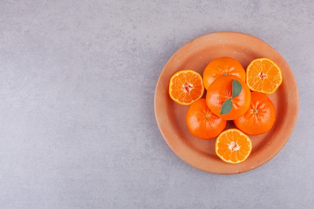 Foto frutas inteiras de laranja com tangerinas fatiadas colocadas em prato de barro.