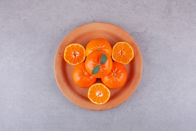 Frutas inteiras de laranja com tangerinas fatiadas colocadas em prato de barro.