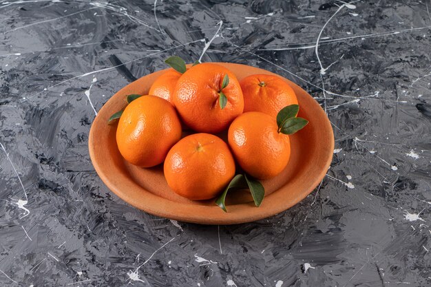 Frutas inteiras de laranja frescas com folhas colocadas em prato de argila