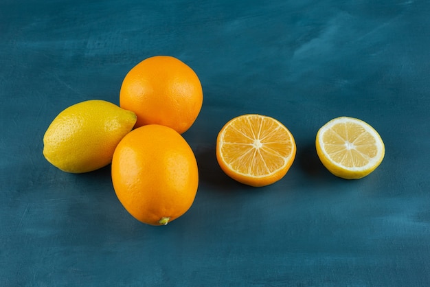 Frutas de limón enteras y en rodajas colocadas sobre una mesa azul oscuro.