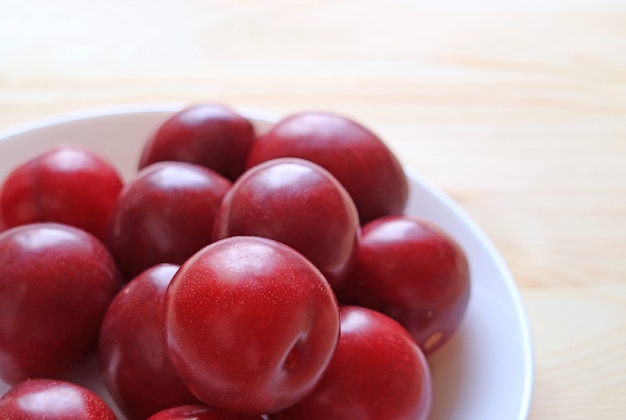 Frutas maduras del ciruelo de Ruby del golfo del color rojo amontonadas en la placa blanca servida en la tabla de madera