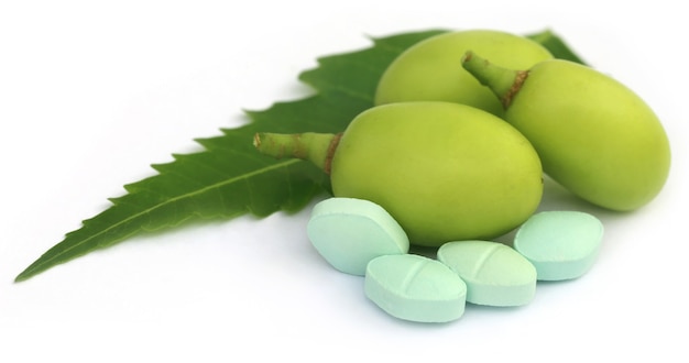 Frutas medicinais de nim com comprimidos sobre fundo branco