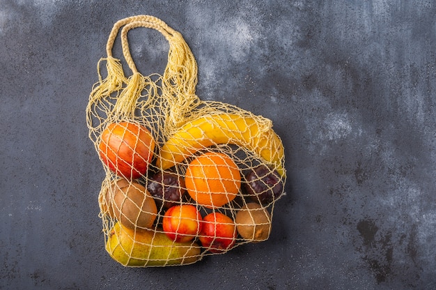 Foto frutas na linha em saco de barbante amarelo eco em superfície de madeira escura