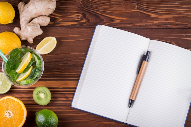 Foto frutas orgánicas frescas y cuaderno y bolígrafo en blanco abierto sobre fondo de madera. concepto de comida sana y vida sana. vista superior