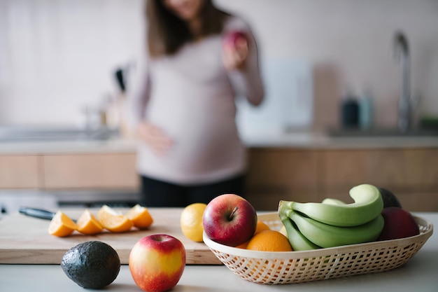 Foto frutas orgânicas frescas e saudáveis no balcão da cozinha com uma jovem asiática grávida sorridente a tocar a barriga e a comer uma maçã na cozinha em casa a comer bem