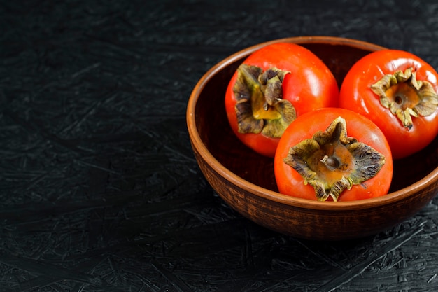 Frutas de otoño Caqui sobre una superficie de madera negra. Caquis en un plato de arcilla.