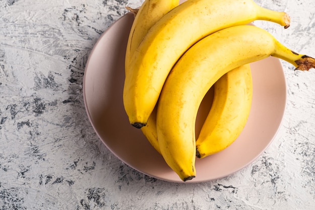 Frutas de plátano en placa rosa sobre fondo blanco con textura, vista superior copia espacio