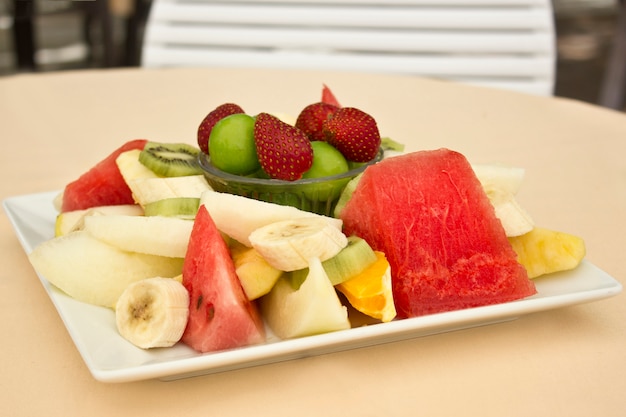 Foto frutas en un plato. ciruela verde, fresa, plátano, kiwi, sandía, naranja y manzana.