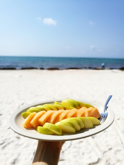 Foto frutas en un plato en la playa contra el cielo