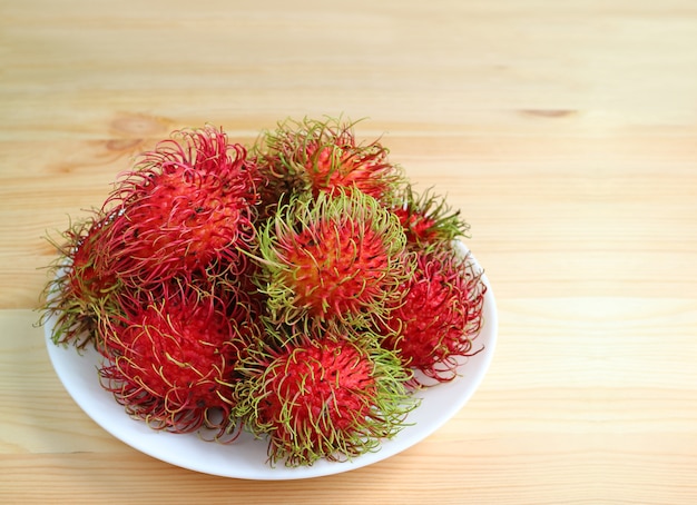 Frutas de Rambutan maduras rojas vibrantes apiladas en un plato blanco en mesa de madera