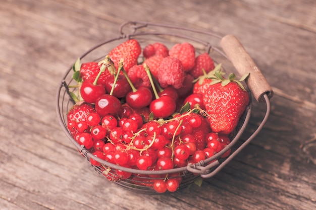 Frutas rojas de verano en canasta de metal sobre la mesa