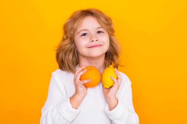 Frutas saludables para niños Niño con naranja y limón en estudio Retrato de estudio de niño lindo sostener limón y naranja aislado sobre fondo amarillo