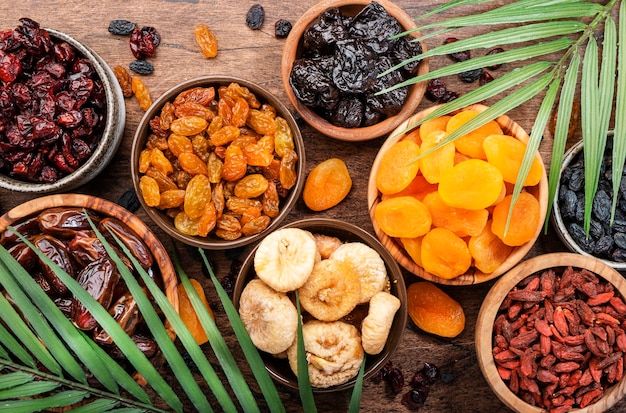 Frutas secas naturales en tazones Comida saludable bocadillos secados al sol mezcla orgánica de albaricoques higos pasas dátiles y otros en la vista superior de la mesa de madera