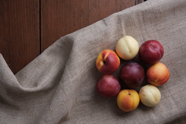 Frutas suculentas em uma toalha de mesa de linho sobre uma velha mesa de madeira. Damascos de ameixa em um fundo vermelho escuro