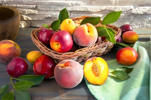 Frutas suculentas maduras doces, pêssegos, ameixas, marmelos, damascos com folhas verdes em uma cesta sobre um fundo escuro de madeira sobre uma tábua