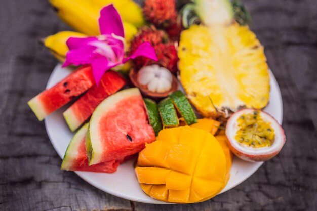 Frutas tropicais coloridas no prato grande na vista superior de fundo de madeira rústica