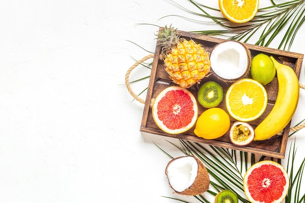 Frutas tropicais e folhas de palmeira em um fundo branco, vista superior.