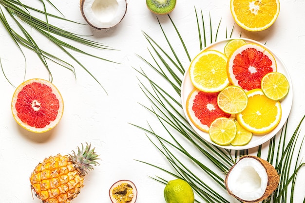 Frutas tropicais e folhas de palmeira em um fundo branco, vista superior.