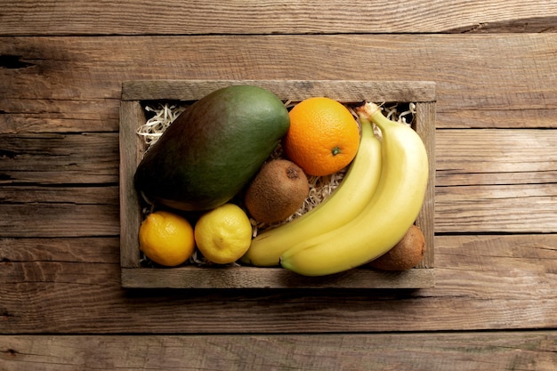 Foto frutas tropicais frescas em uma caixa de entrega de madeira sobre uma mesa de madeira. laranja, banana, manga, kiwi e limão, vista superior.