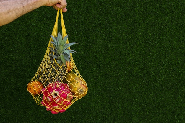 Frutas tropicais: manga, mamão, abacaxi, dragão e maracujá em uma sacola têxtil amarela sobre fundo verde, orientação horizontal, espaço de cópia