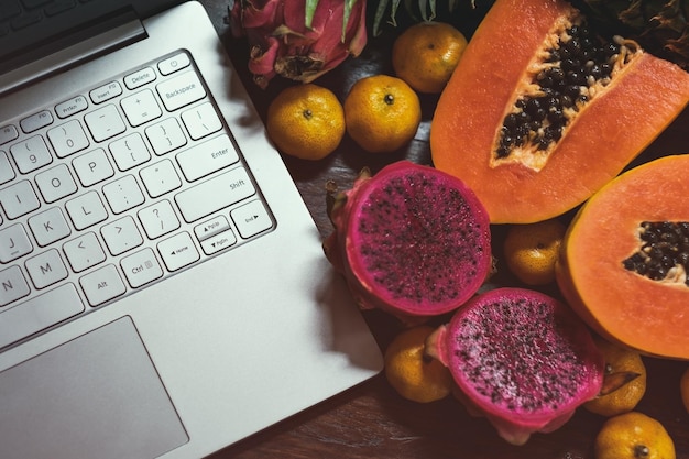 Foto frutas tropicais perto de laptop moderno em fundo de madeira estilo de vida vegano