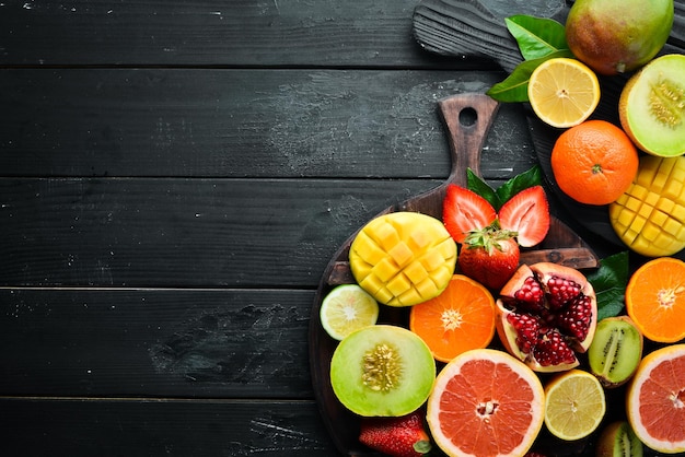 Frutas tropicales frescas sobre un fondo negro. Cítricos, melón, granada, fresa, plátano. Vista superior. Espacio libre para su texto.