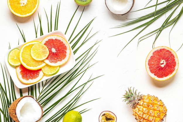 Frutas tropicales y hojas de palma sobre un fondo blanco.