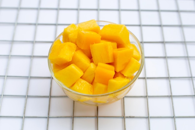 Frutas tropicales, rodajas de cubo de mango en un tazón de vidrio sobre fondo blanco.