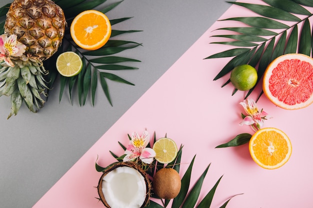 Frutas de verano. Hojas de palma tropicales, piña, coco, pomelo, naranja y limón sobre fondo rosa.