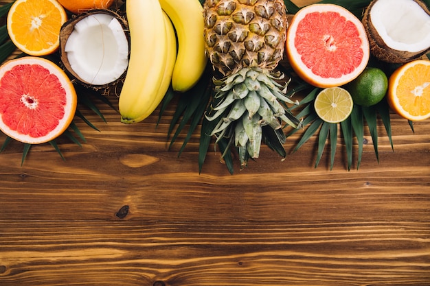 Frutas de verano. Hojas de palma tropicales, piña, coco, pomelo, naranja y plátanos sobre fondo de madera.