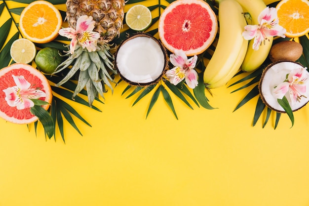 Frutas de verano. Hojas de palma tropicales, piña, coco, pomelo, naranja y plátanos sobre fondo rosa.