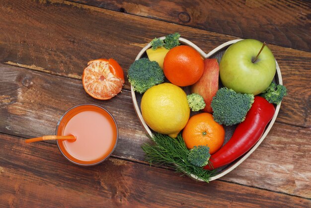 Frutas y verduras en caja de madera en forma de corazón. Brócoli, manzanas, pimientos, mandarinos.