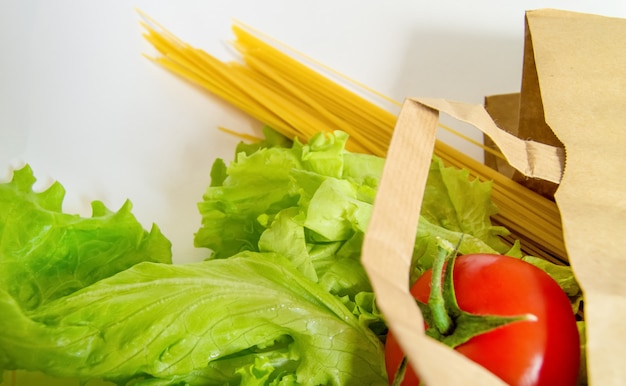 Frutas y verduras crudas, pasta enrollada de una bolsa de papel en una pared blanca, conceptos de compra, entrega de alimentos.