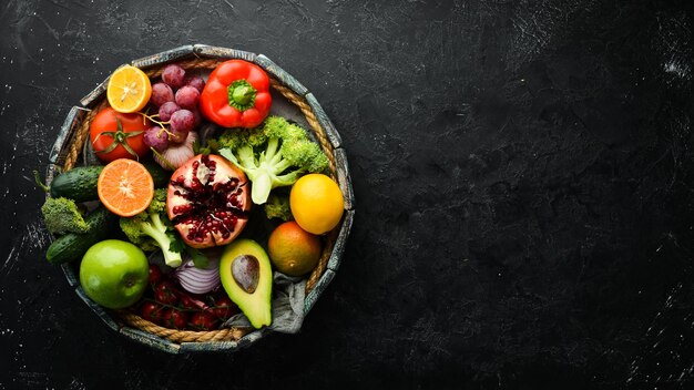 Frutas y verduras maduras en caja de madera Frutas y verduras sobre fondo de piedra negra Frutas tropicales Vista superior Espacio libre para el texto