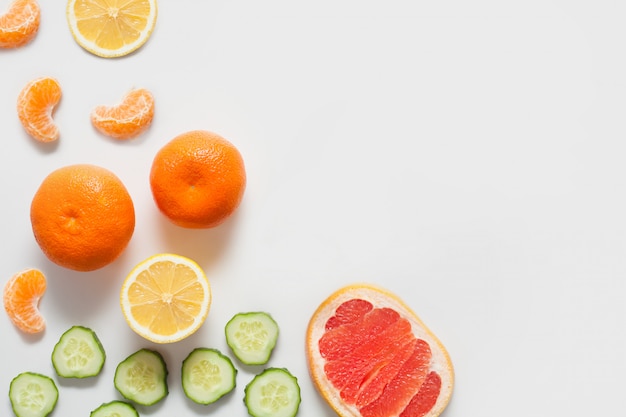 Frutas y verduras en una pared blanca, incluyendo cítricos limón y mandarinas, pomelo y pepino fresco en rodajas. concepto de vitaminas, alimentos saludables, paredes para supermercados.